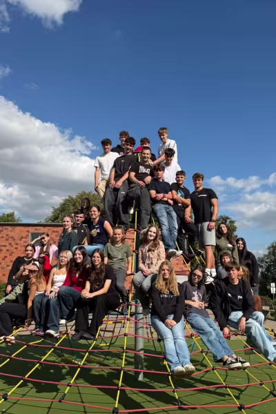 Fotografia: Duża grupa uśmiechniętych młodych ludzi na siatce wspinaczkowej na zewnątrz.