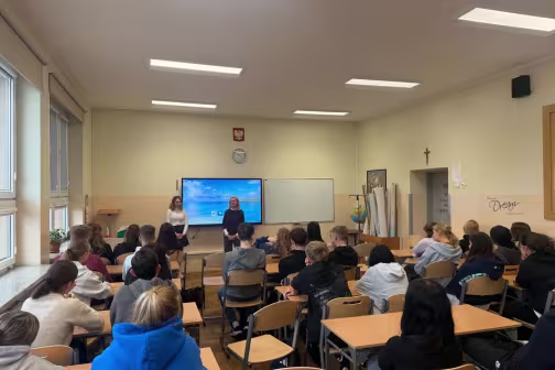 Klasa szkolna z uczniami słuchającymi prezentacji dwóch kobiet.