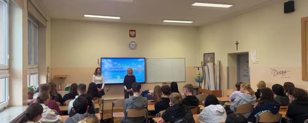 Klasa szkolna z uczniami słuchającymi prezentacji dwóch kobiet.